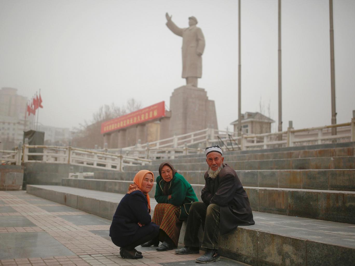 Ethnic Uighurs sit near a statue of China's late Chairman Mao Zedong in Kashgar, Xinjiang Thomas Peter/Reuters