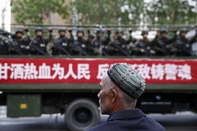A Uyghur man looks on as a truck carrying paramilitary policemen travels along a street during an anti-terrorism oath-taking rally in Urumqi, Xinjiang (May 23, 2014).